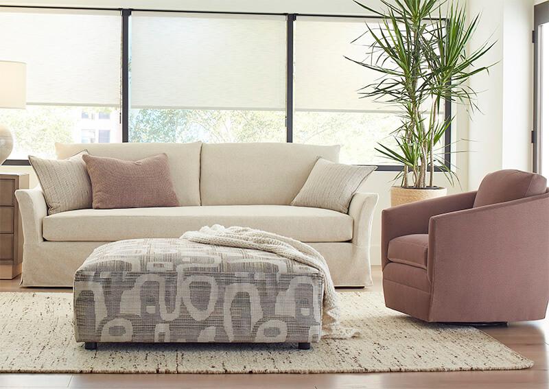 a cream sofa with a lavender accent pillow next to a lavender swivel chair